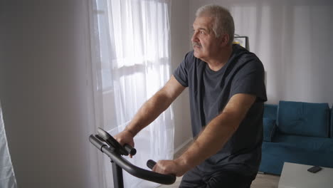 middle-aged-man-is-training-at-home-spinning-pedals-of-exercise-bicycle-in-living-room-healthy-lifestyle-and-keeping-good-physical-condition-at-middle-age